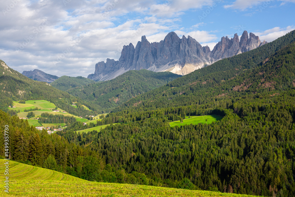 Obraz premium Picturesque landscapes of alpine highland valley of Val di Funes located at foot of rocky mountains of Italian Dolomites with green meadows, dense forests and charming rustic houses on sunny day