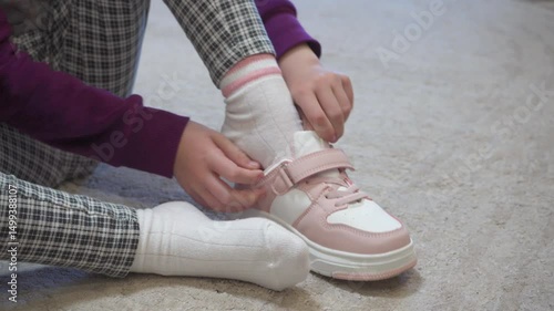 a little girl puts on sneakers on the carpet, sneakers, leg, putting on shoes, plaid pants, indoors, pants, fashion, putting on shoes, couple, kindergarten, sitting, little, girl, sneakers, child, foo
