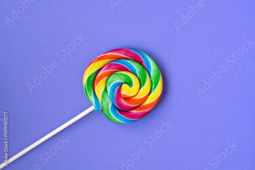Colorful rainbow swirl lollipop on a solid purple background. Playful and sweet concept representing childhood, sugar, and vibrant summer energy