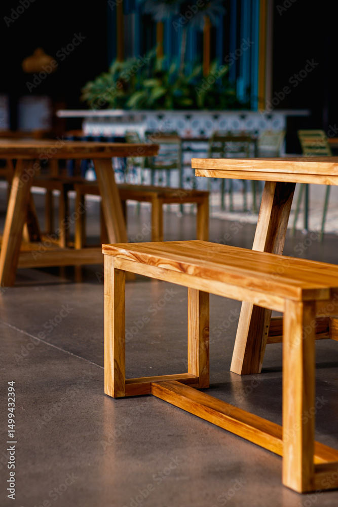 Fototapeta premium Clean lines of modern wooden benches and tables in a contemporary cafe or eatery. Warm wood tones contrast with cool polished concrete floors, creating an inviting, minimalist interior space.