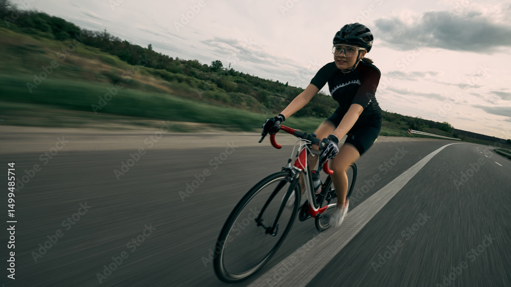 Fototapeta premium Motion blur photo of cyclist speeding through countryside, strong pedaling movement, concentration on face, asphalt blurred into horizon. Concept of velocity, drive, strength, competition.
