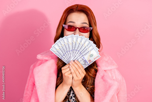 Wealthy young woman holding money with stylish outfit on a pink background showing sophistication and success