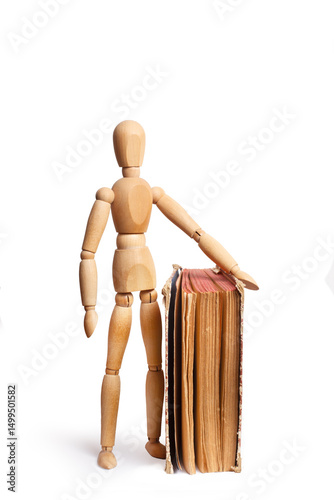 A wooden mannequin standing close to a book isolated on a white background