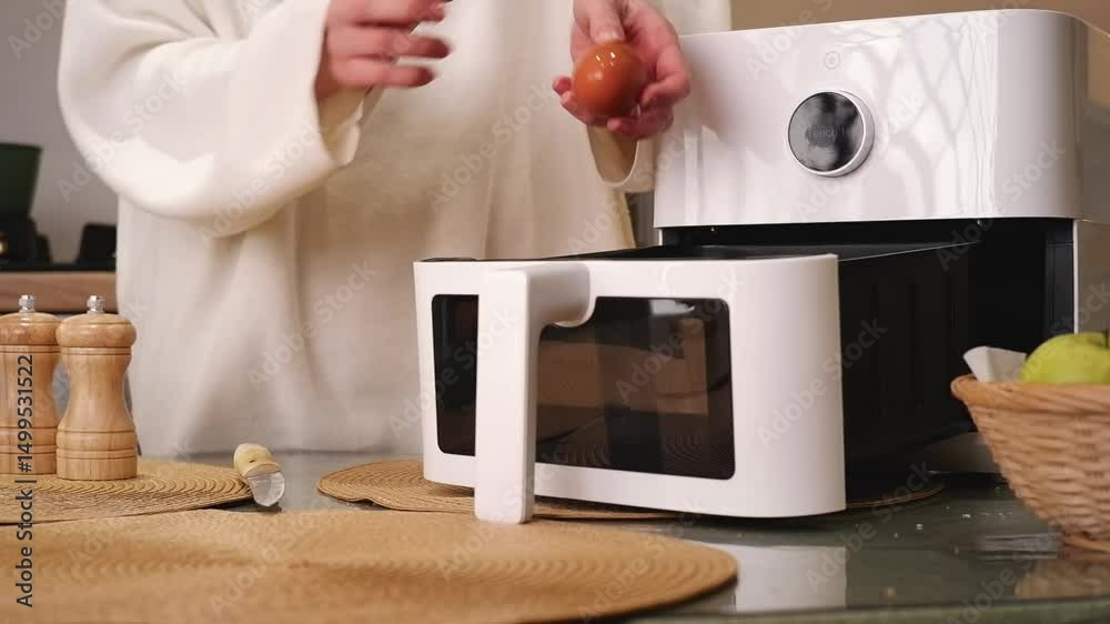 Woman putting parchment paper in air fryer basket, cracking an egg and setting temperature