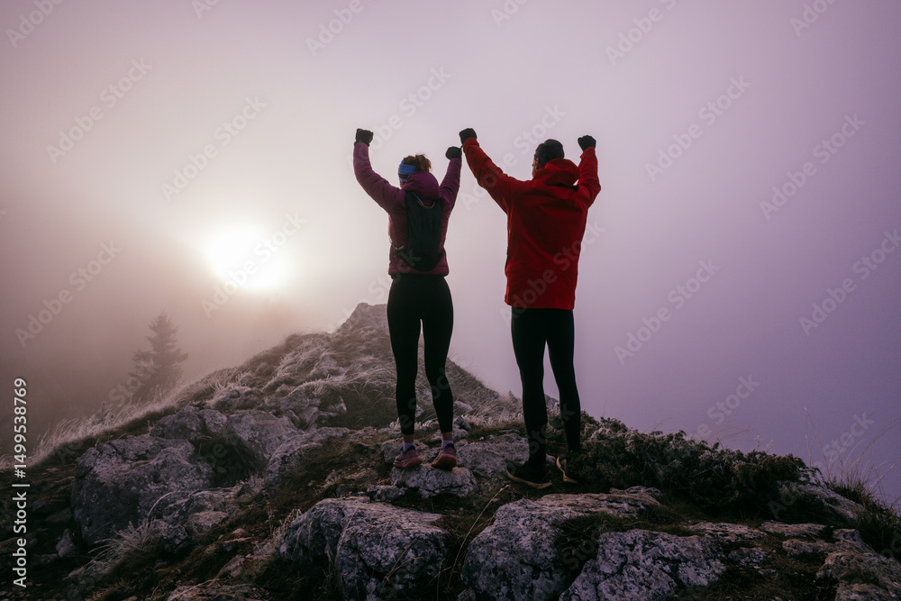 Obraz premium Two Hikers Celebrating on Rocky Peak.Couple hikers raising fists on rugged mountain ridge at sunrise.