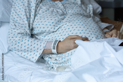 Pregnant woman resting in hospital bed touching belly