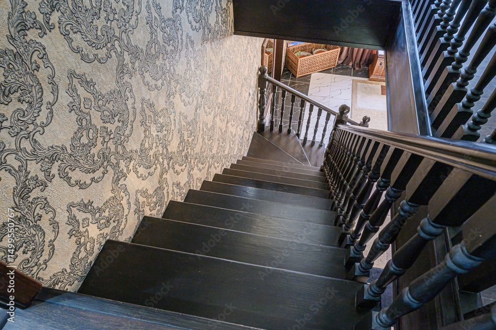 Obraz premium high-angle shot of a dark wooden staircase descending. An ornate patterned wallpaper adorns the adjacent wall, offering a contrast to the staircase