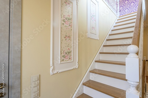 interior shot of a stairway with floral wall art on the light yellow wall. The stairway has wooden steps and white railings