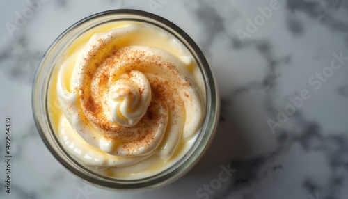 Creamy zabaione dessert in glass. Top view close-up of Italian custard dessert. Whipped egg yolk mousse with cinnamon spice. Culinary delight on white marble. Sweet, rich, delicious.