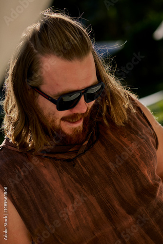Portrait of a long haired bearded man in a brown t-shirt and sunglasses chilling in the hotel.