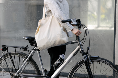 Woman holding eco bag or cotton tote bag in the city while riding a bike