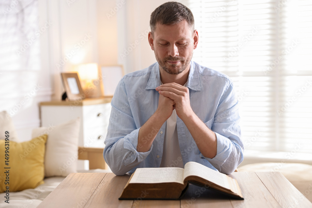 Fototapeta premium Man with Bible praying at table indoors