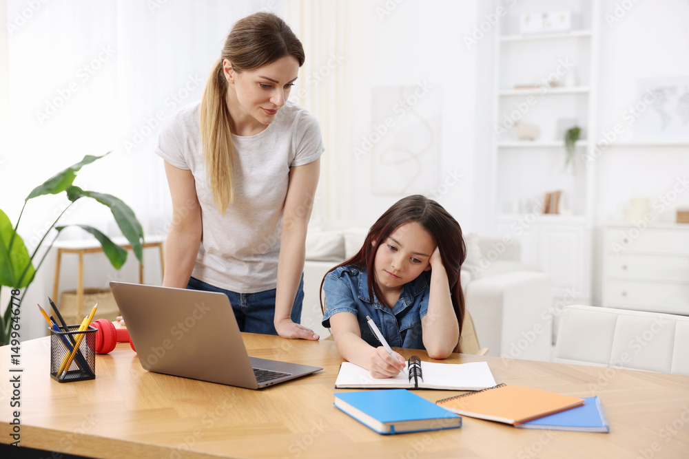 Mother helping her daughter with homework at wooden table indoors Mother helping her daughter with homework at wooden table indoors