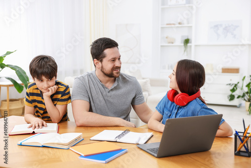 Father helping his kids with homework at wooden table indoors
