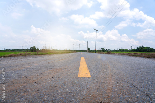 Fototapeta Naklejka Na Ścianę i Meble -  Rural small two lane asphalt road through rice fields there are power lines along roadside and solar street lights sky white clouds after rain in countryside Nakhon Pathom Thailand.