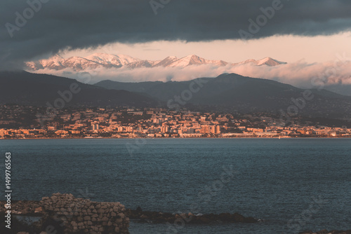 view of snowy alps and city of nice, in french riviera, at golden hour time with moody clouds