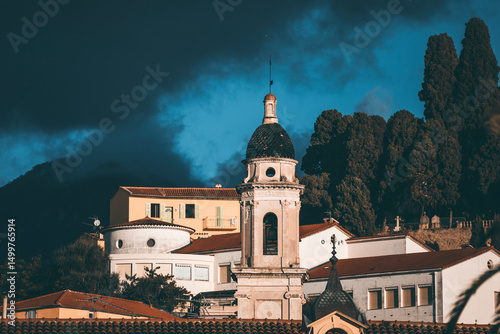 bell tower detail in the old town of mentone, in french riviera, with blue sky and high contrast light, and dark mountains background