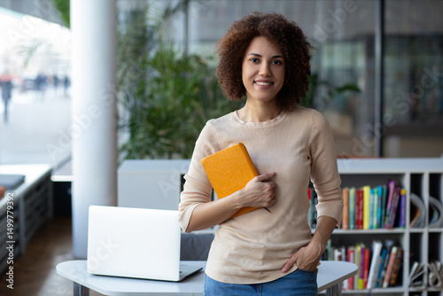 Attractive young female university student using a laptop while studying in the library, modern education