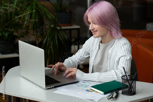 Young modern woman freelancer or entrepreneur working remotely using laptop while sitting in coworking space