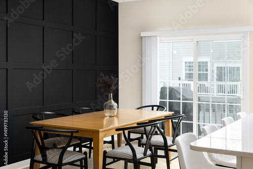 Obraz na plátne A cozy dining room with a wainscoting wall, wooden dining room table surrounded by black chairs, bar stools sitting at an island and a bright doorway