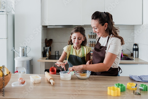 hispanic mother and little daughter baking in kitchen at home 