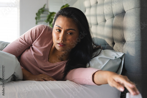 Woman in bed reaching for alarm clock, waking up in morning