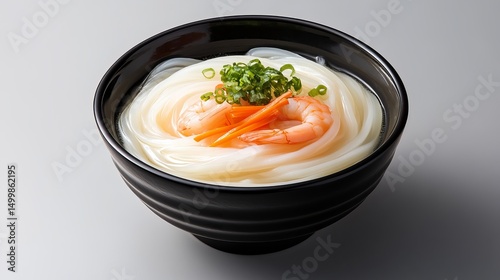 Udon noodles are served in a black bowl, garnished with shrimp, carrots, and green onions.