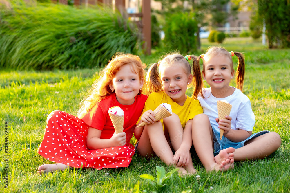 Fototapeta premium happy children eating ice cream in the summer on the green lawn in the park, a bright summer photo of children's holidays, three baby girls laughing and having fun in the summer