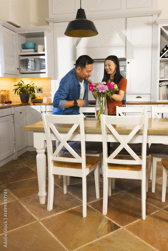 Mature Asian couple arranging flowers in vase, smiling together in cozy kitchen Mature Asian couple arranging flowers in vase, smiling together in cozy kitchen