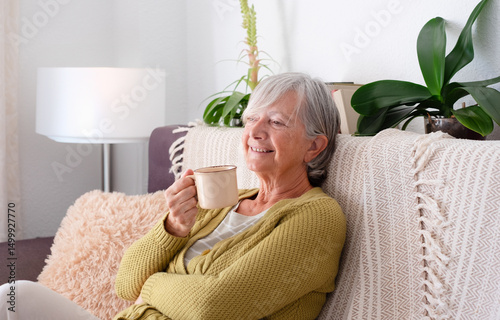 Slika na platnu Smiling Senior Woman Sitting Indoors in Cozy Sofa having a relaxing moments enjoying a cup of coffee