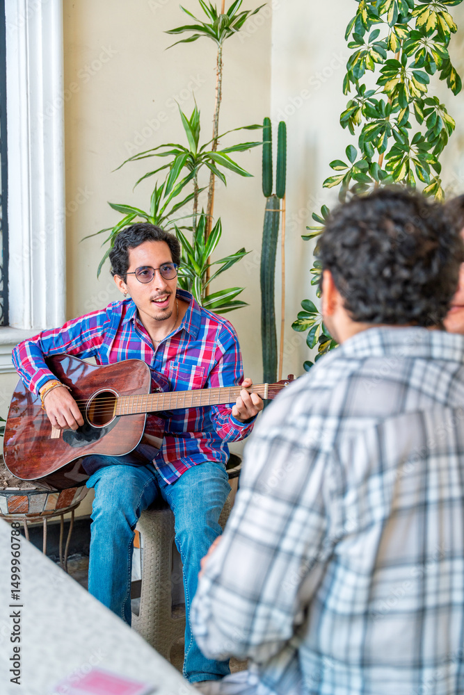 Fototapeta premium Young man playing acoustic guitar for friends at home gathering
