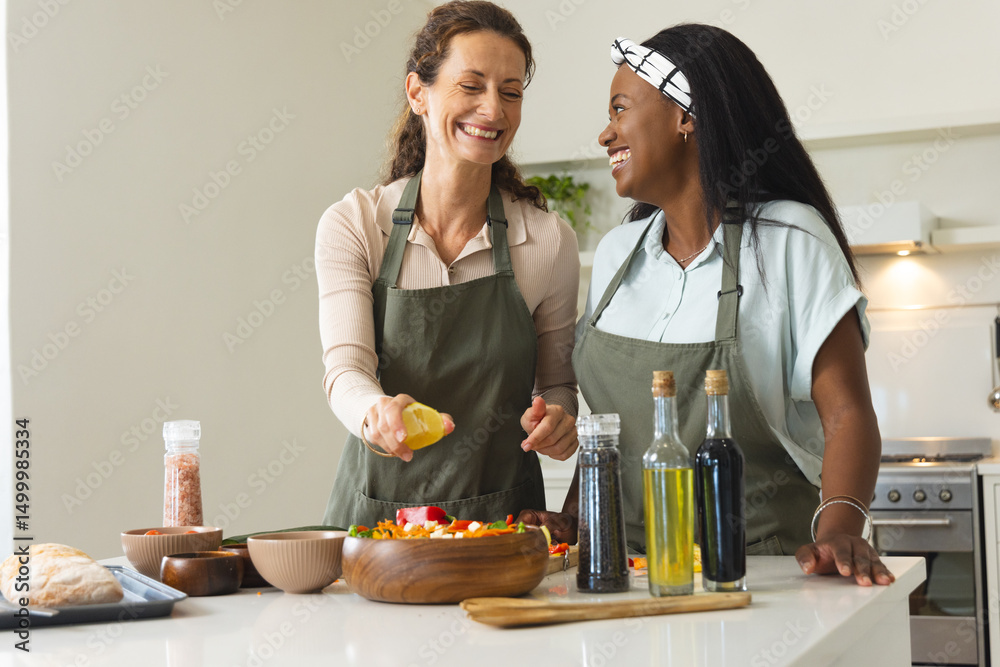 Diverse female friends preparing salad in home kitchen, with wooden bowl and dressing bottle Diverse female friends preparing salad in home kitchen, with wooden bowl and dressing bottle