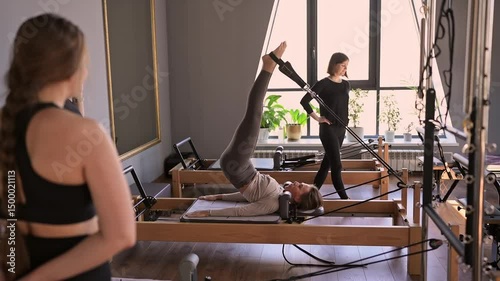 Woman training pilates on the reformer bed. Reformer pilates studio machine for fitness workouts in gym. Fit, healthy and strong authentical body. Fitness concept