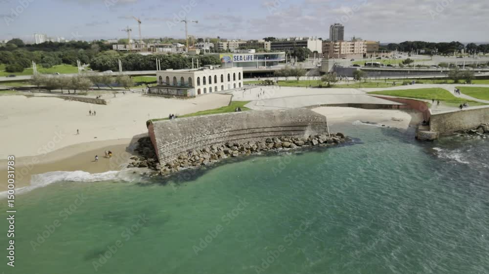 Drone flies up and away from the Pontão do Castelo do Queijo at the Praia Internacional on a sunny afternoon in Porto, Portugal