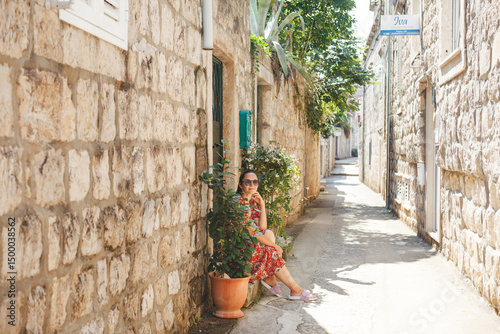 Wallpaper Mural A beautiful woman walks along a charming alley with rustic stone walls, flowering plants and the overall serene atmosphere of the Old Town in Croatia Torontodigital.ca