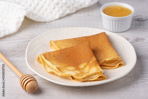 Traditional Russian pancakes with honey on a white wooden table