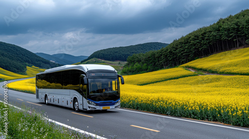 A large white bus is driving down a road with a yellow field in the background