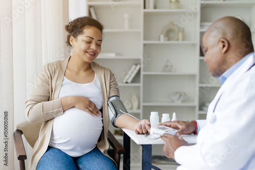 Doctor Wearing Uniform Measuring Blood Pressure For Black Pregnant Female Patient, Therapist Man Checking Hypertension Of Smiling Expectant Woman During Medical Checkup In Modern Clinic