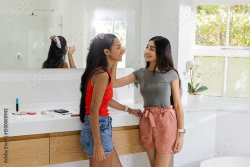 Applying makeup teenage friends standing by bathroom sink, with makeup brush and eyeshadow palette