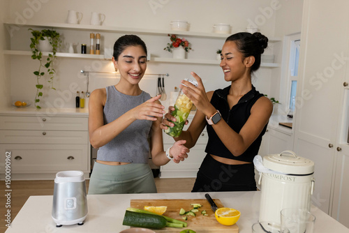 Blending diverse female friends mixing fruits and greens in white kitchen, with blender jar photo