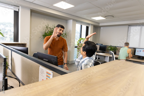 High-fiving diverse male coworkers celebrating project win in open office, with monitor, copy space photo