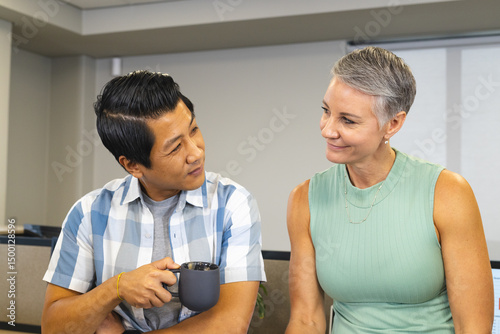Chatting Diverse coworkers sitting in modern office cubicle area, with dark ceramic coffee mug