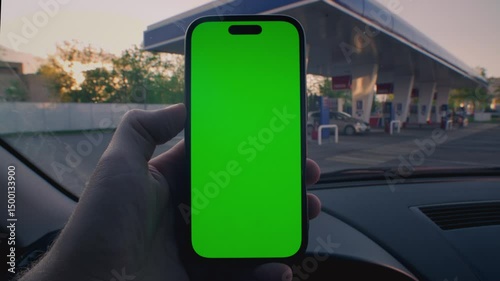 Man driver is holding smartphone, green screen for chroma key in hand, touching finger. Gas station