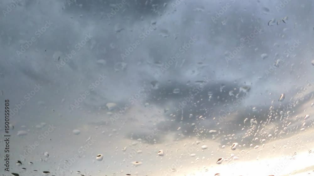 Nahaufnahme von Regentropfen, die an einer Fensterscheibe runterlaufen, mit dramatisch dunklen Regenwolken im Hintergrund. Trübe Wetterstimmung, Zeitraffer, Metrologie, Melancholie, Herbst