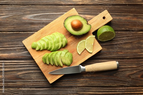 Fotografía Cut ripe green avocado, lime and knife on wooden table, flat lay