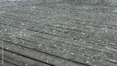 Hailstones pelting gray wooden deck surface, bouncing and creating rhythmic impacts during intense summer storm with raw meteorological energy