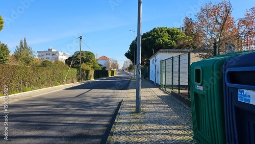 Quiet residential street with recycling containers and green hedges on a sunny day in Portugal