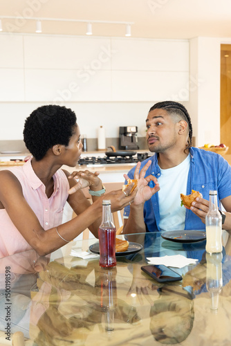 Eating couple talking and gesturing in modern home kitchen, with sandwiches and smartphone photo