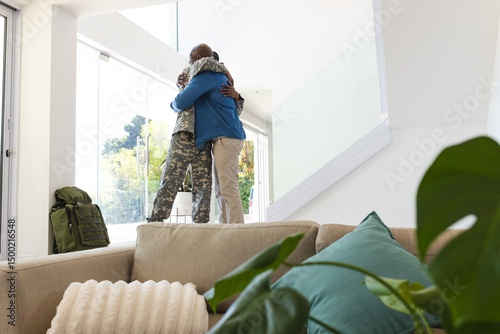 Embracing African American father and son standing by glass door at home, with military backpack