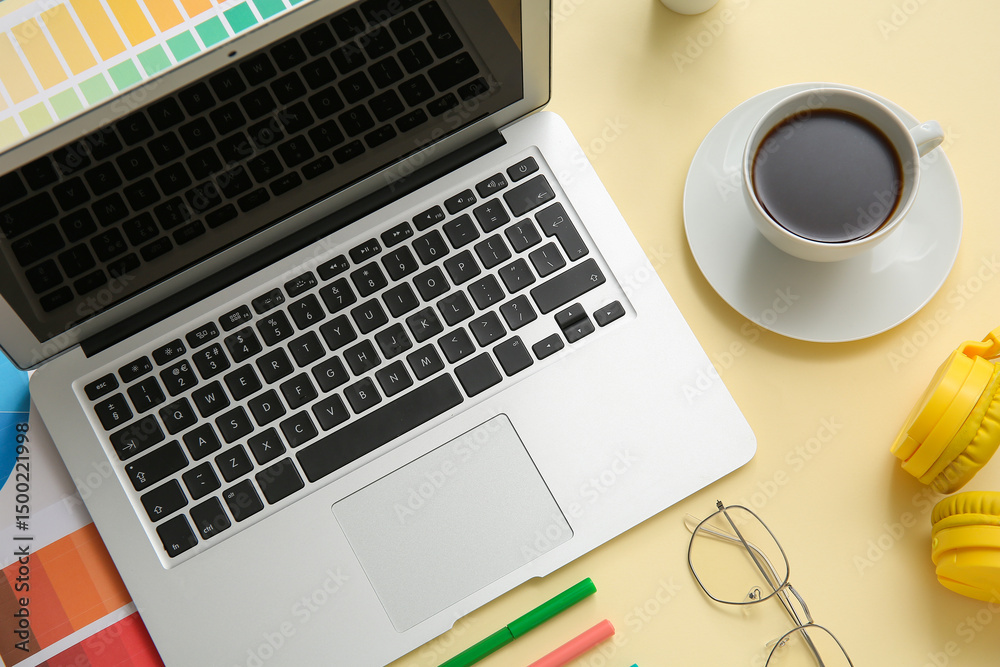 Workplace of graphic designer with laptop, coffee and color charts on yellow background Workplace of graphic designer with laptop, coffee and color charts on yellow background
